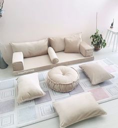 a living room filled with lots of pillows on top of a white floor next to a potted plant