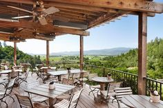 an outdoor dining area with wooden tables and chairs on a deck overlooking rolling hills in the distance