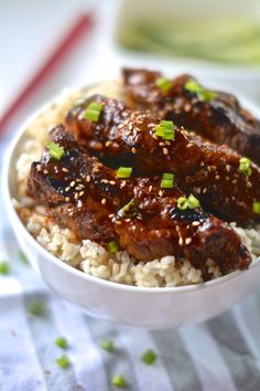 a white bowl filled with rice covered in sauce and green onion garnishments