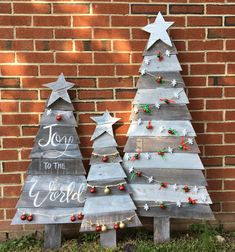 two wooden christmas trees sitting next to each other in front of a brick wall with the words joy to the world written on them