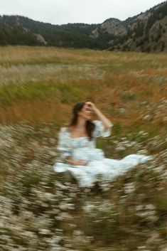 a woman sitting in the middle of a field with wildflowers on her knees