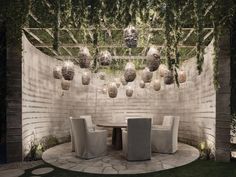 an outdoor dining area with white chairs and greenery hanging from the ceiling above it