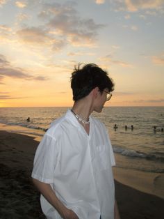 a man standing on top of a sandy beach next to the ocean at sun set