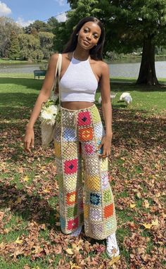 a woman standing in the grass with her hands on her hips and wearing colorful crochet pants