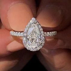 a woman's hand holding an engagement ring with a pear shaped diamond on it