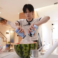 a young man is pouring water into a bowl filled with ice cubes and fruit