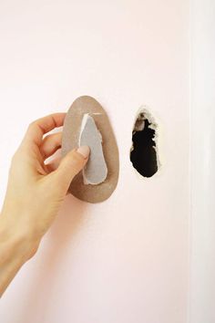 a hand is holding a piece of paper near a hole in the wall