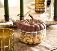 a glass bowl filled with nuts sitting on top of a table next to two candles