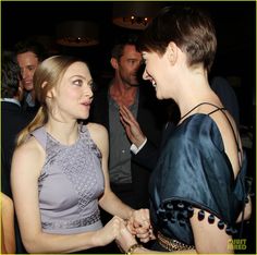 two women talking to each other in front of others at a party with one woman holding the other's hand