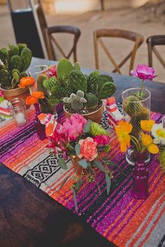 a table topped with potted plants on top of a wooden table covered in colorful cloth