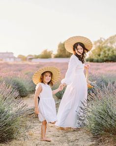 mother and daughter walking in lavender field with straw hats on their heads, holding hands