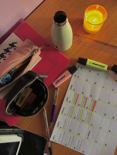 a wooden table topped with lots of office supplies next to a candle and cell phone