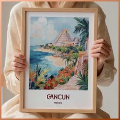 a woman holding up a framed poster with the words cancun in front of her