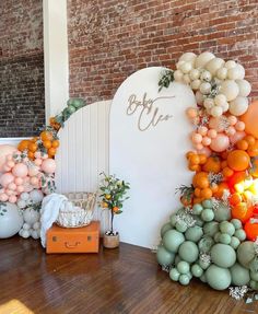 an orange and white balloon arch is displayed in front of a brick wall with other balloons