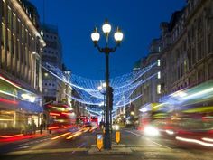 the city street is lit up with christmas lights and double decker buses are passing by