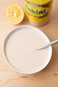 a bowl of yogurt with a spoon next to an orange and a jar of yogurt