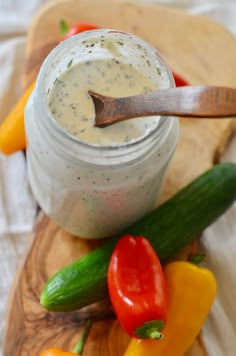 a wooden cutting board topped with assorted veggies next to a jar of dip