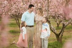 a man and two children standing in front of some trees with pink flowers on it