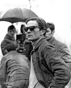 black and white photograph of man with sunglasses holding an umbrella in front of other men