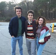 three people standing next to each other in front of a parking lot with trees behind them