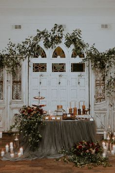 a table with candles and greenery on it in front of a white door that is decorated with ivy