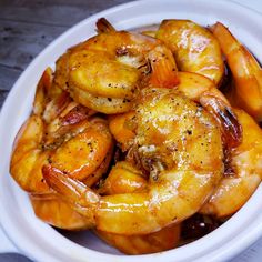 a white bowl filled with cooked shrimp on top of a wooden table