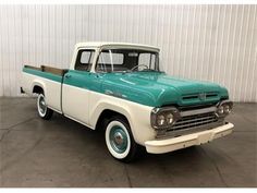 an old green and white pickup truck parked in a garage with a wall behind it