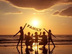 four people standing on the beach with their arms in the air and one person holding up a sign that says family