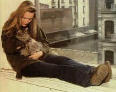 a woman sitting on a window sill holding a cat