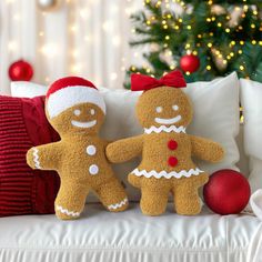 two stuffed gingerbreads sitting on a couch next to a christmas tree