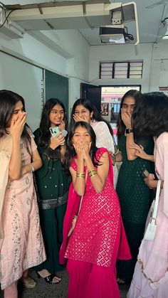 a group of women standing next to each other in front of a mirror with one woman covering her mouth