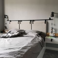 an unmade bed with two lamps on each side and a white wall behind it