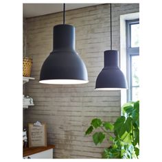 two gray lamps hanging from the ceiling in a room with brick wall and potted plant