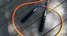 an orange jump rope attached to a black and silver device on a wooden deck with two handles