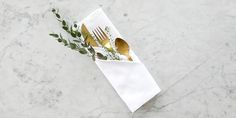 a fork and knife in a white napkin on a marble counter top with greenery