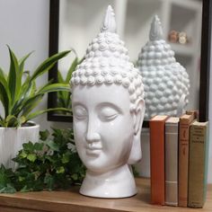 a white buddha head sitting on top of a wooden table next to books and plants