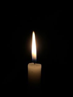 a lit candle in the dark with only one light on it's side,