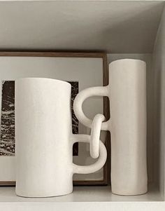 two white coffee mugs sitting on top of a shelf next to a framed photo