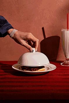 a person placing a piece of food on top of a white plate with a red table cloth