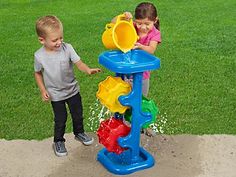 two young children playing in a water sprinkler on the ground near grass