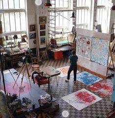 a person standing in an art studio with lots of paintings on the walls and floor