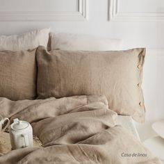 an unmade bed with two pillows and a tea pot on the end table next to it