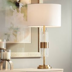 a table lamp sitting on top of a white dresser next to a painting and candle