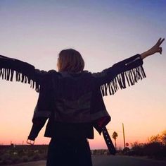 a woman with her arms spread out in the air while standing on a road at sunset