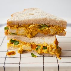 two halves of a sandwich sitting on top of a white tiled counter next to a knife