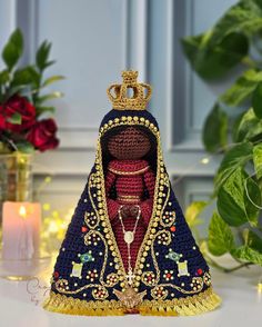 a crocheted figurine with a crown on it's head sitting next to flowers