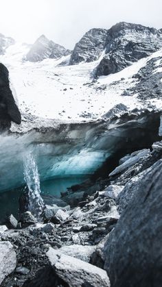 an ice cave in the mountains with water coming out of it and snow on the ground