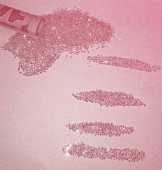 pink glitter next to a tube of lipstick on a white surface with the word love spelled in it