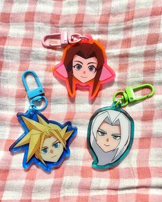 three cartoon keychains on a checkered blanket, one with an anime character