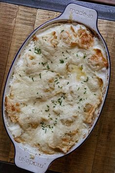 a casserole dish with cheese and herbs in it sitting on a wooden table